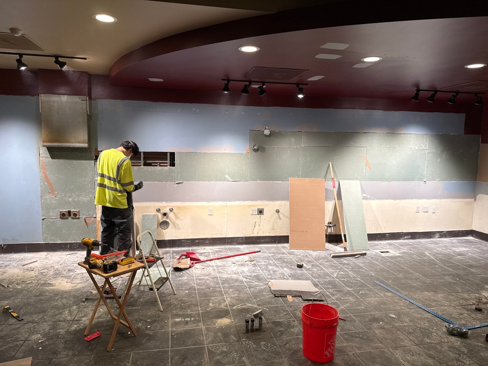 Technician in a high-visibility vest preparing the tile floor of a commercial space during a renovation